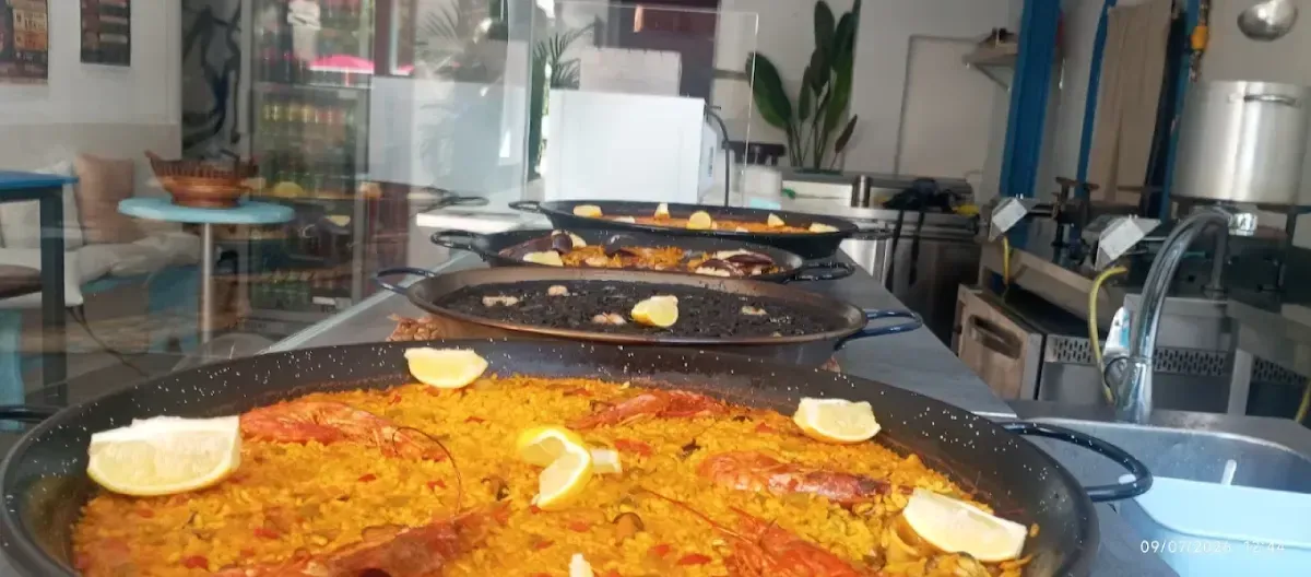 Grandes paelleras cocinándose en una estufa en la luminosa cocina de un restaurante.