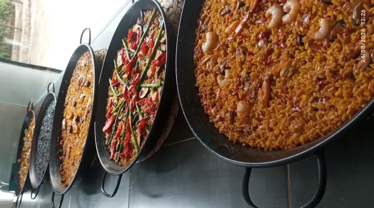 Grandes paelleras negras con arroz, mariscos y verduras en un mostrador tipo bufé.