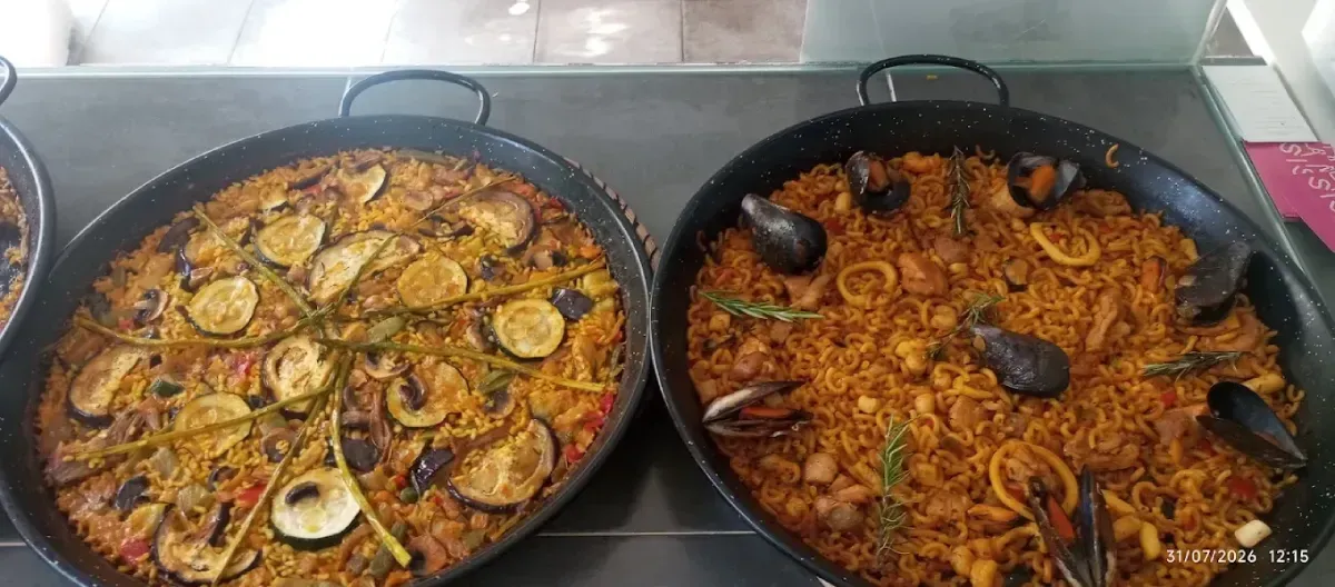 Dos paelleras cocinadas con mariscos y verduras en una estufa.