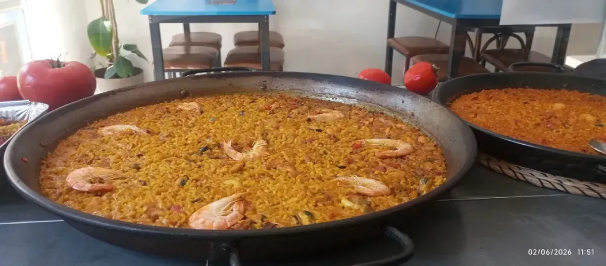 Grandes sartenes de arroz amarillo con mariscos en una mesa de buffet.