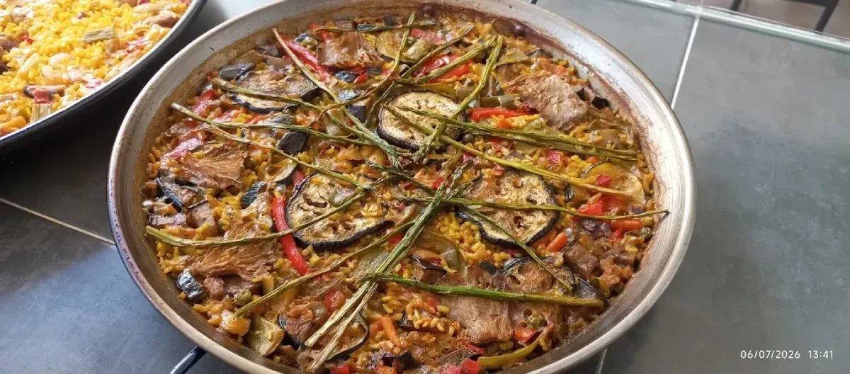 Dos paelleras redondas de colores con paella cocida, arroz, mariscos y verduras sobre una mesa.