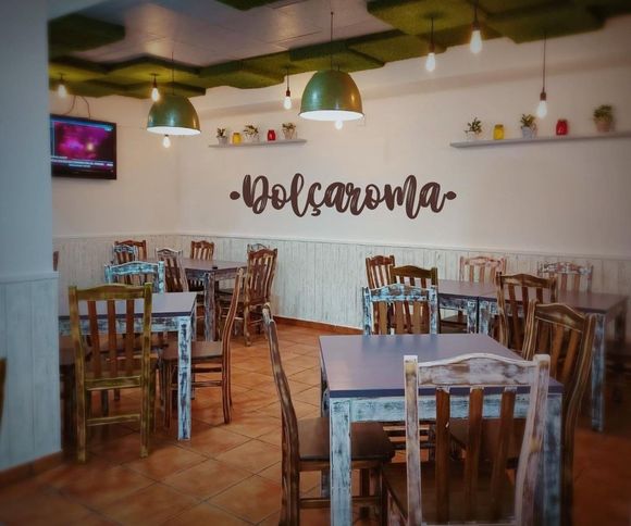 Interior de un café rústico vacío con mesas y sillas de madera, lámparas colgantes verdes y la palabra