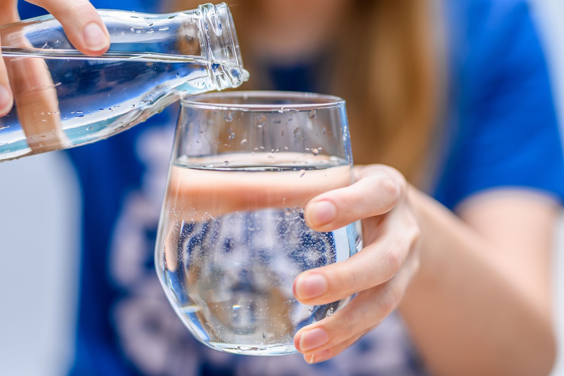 Une femme verse l'eau d'une bouteille en verre dans un verre transparent.