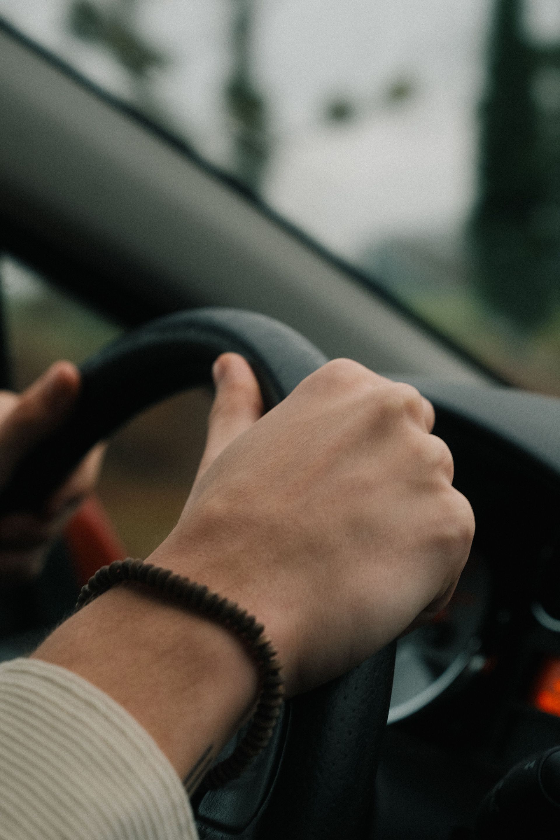 Un SUV blanc roule vers la caméra sur une route urbaine mouillée, avec des voitures garées et des montagnes en arrière-plan.