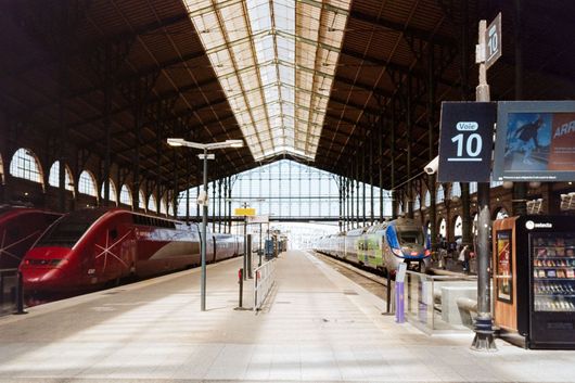 Quai de gare moderne avec un train à grande vitesse rouge sous une grande voûte