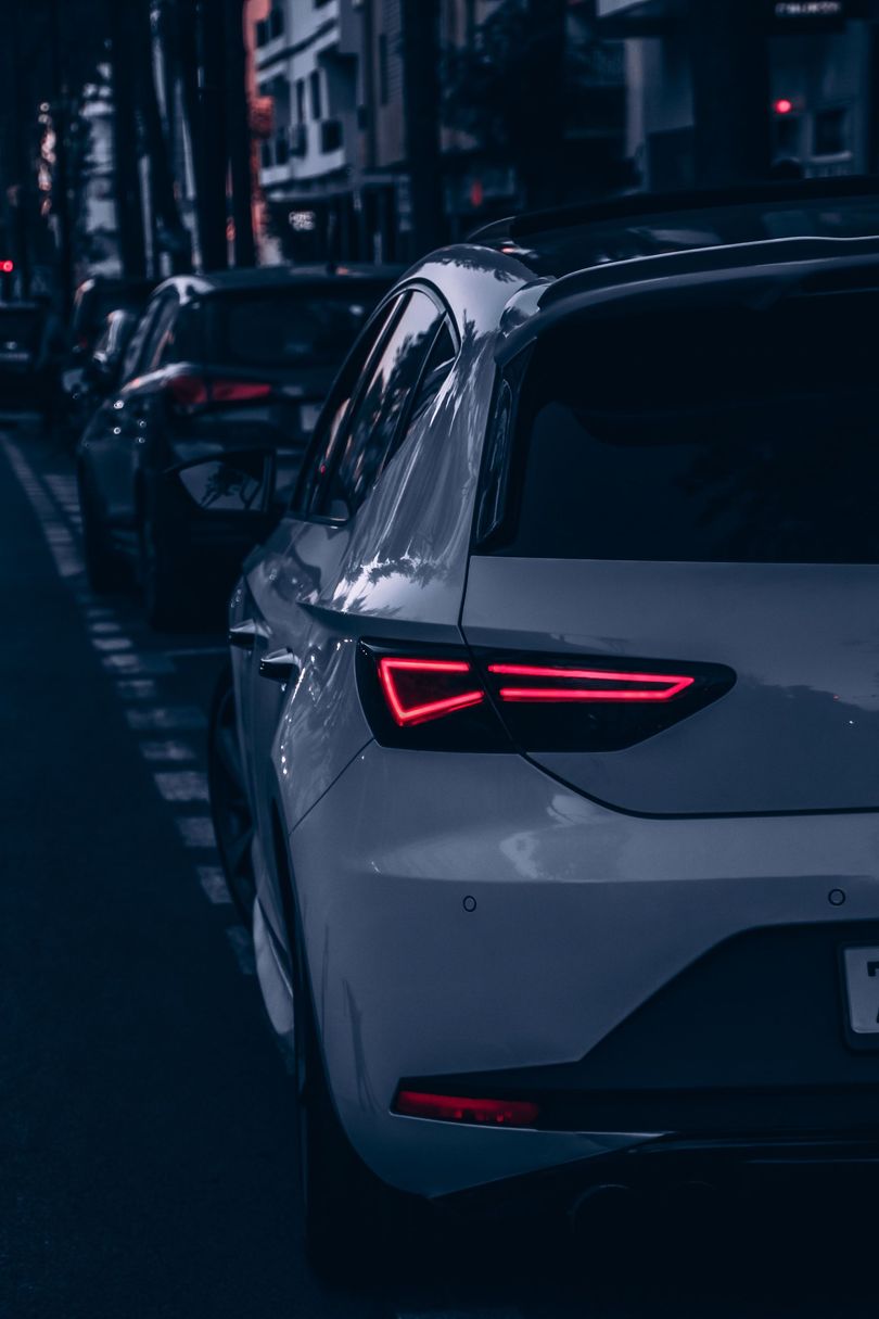 Voiture sombre garée dans une rue pluvieuse de la ville, la nuit, feux arrière rougeoyants.