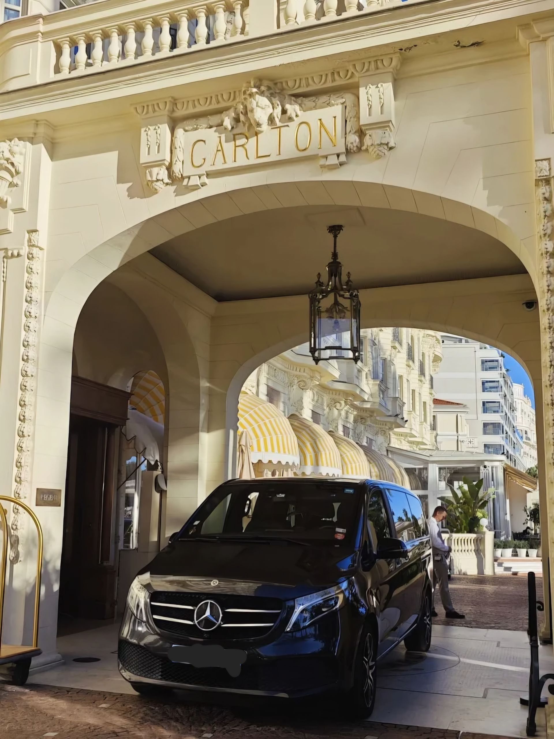 Une camionnette Mercedes noire sous l'arche de l'hôtel Carlton, avec une lanterne suspendue au-dessus.