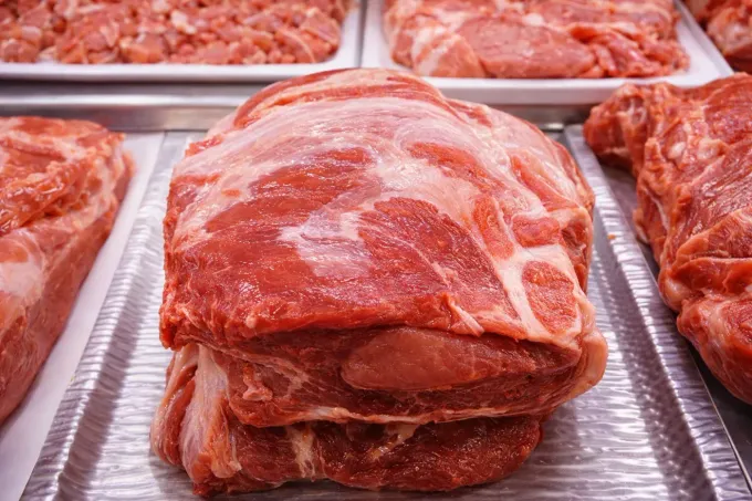 Cortes de carne de cerdo cruda, de varios tamaños, exhibidos en una bandeja de metal, estilo carnicería.