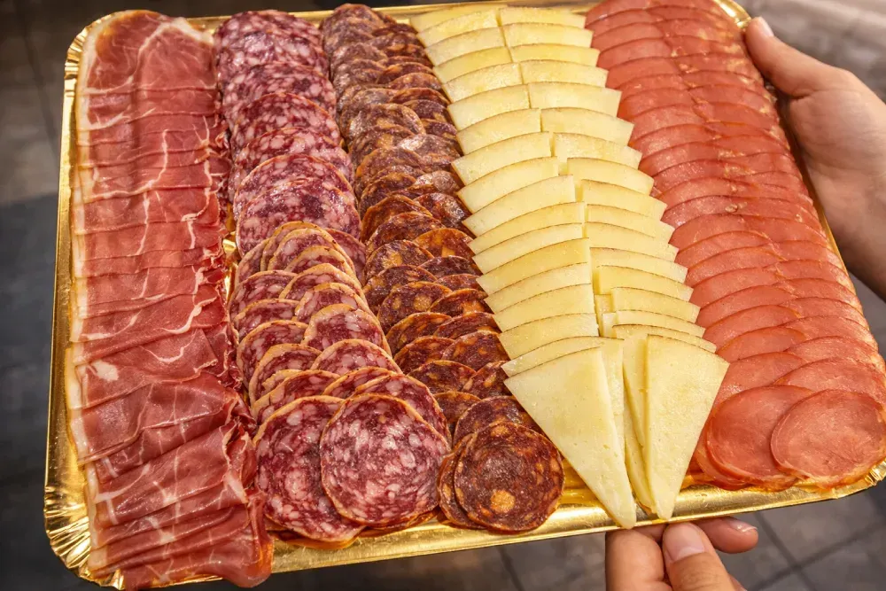 Bandeja de lonchas de carne y queso, sostenida con las manos. Incluye prosciutto, salami, chorizo, queso y pepperoni.
