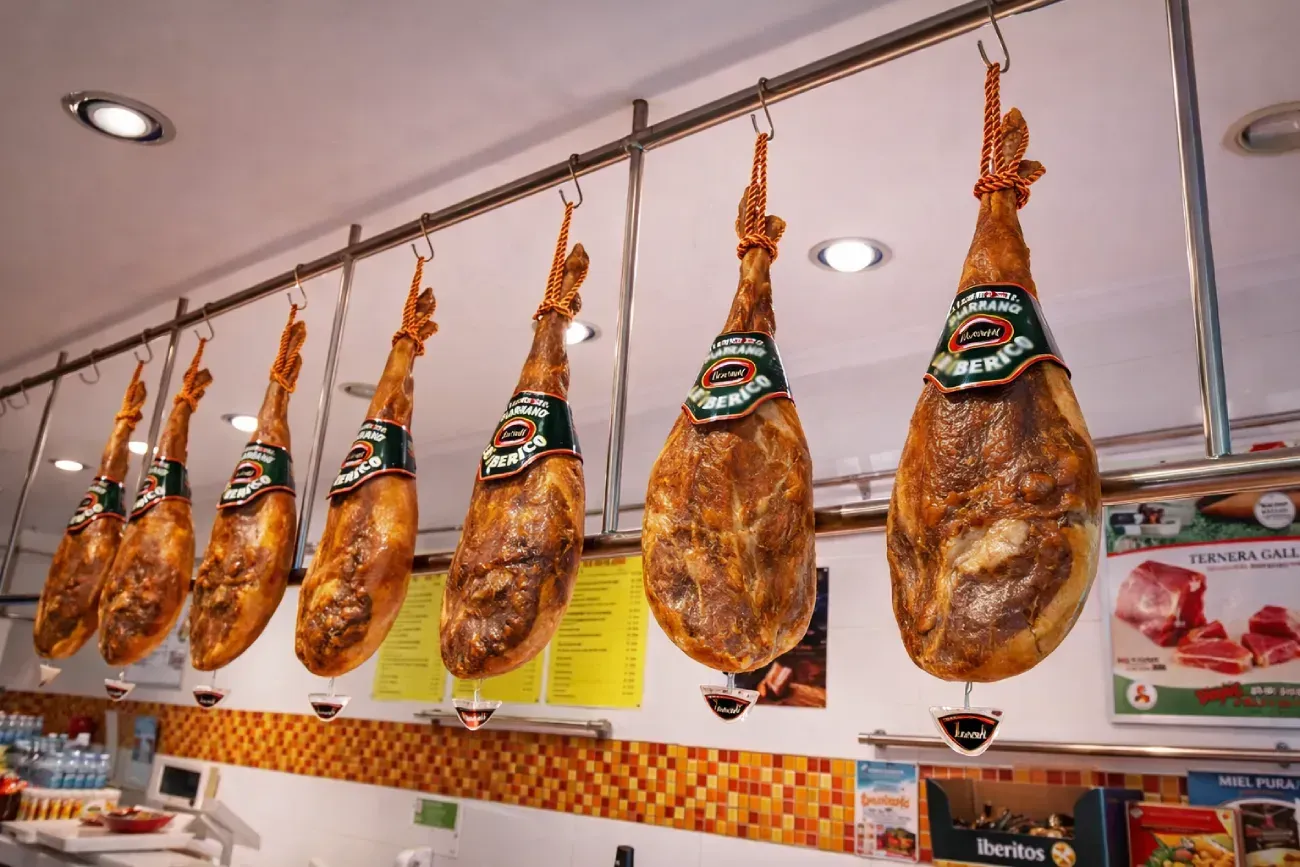 Patas de jamón ibérico curado colgadas en una carnicería, de color marrón y con etiquetas.