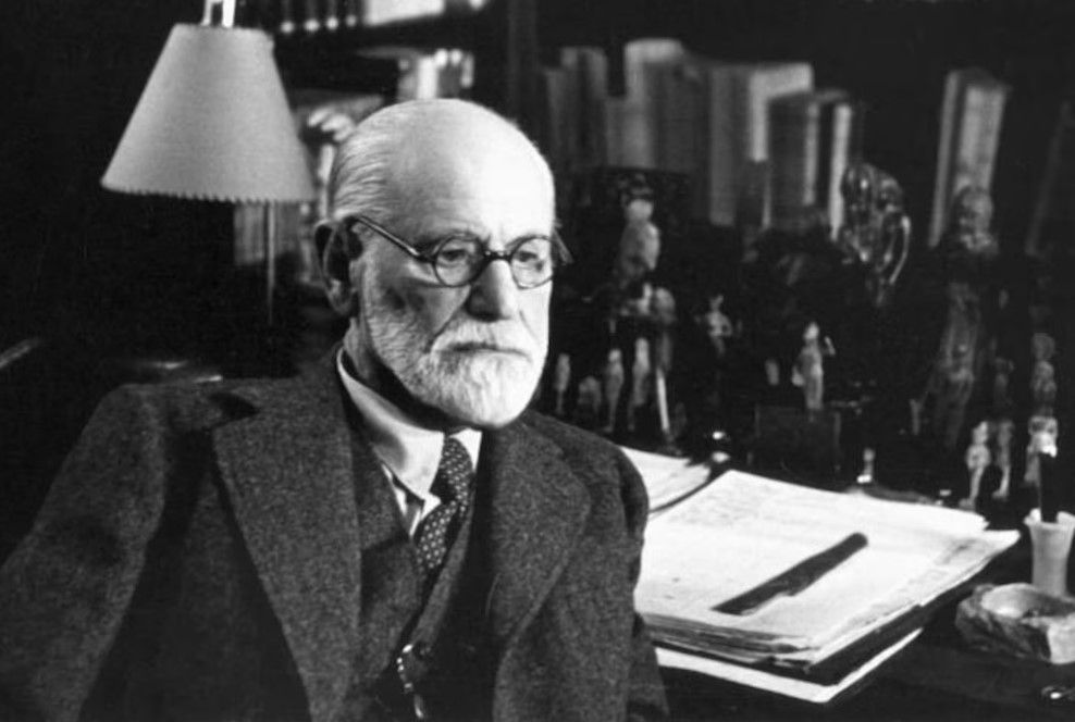 Sigmund Freud dans son cabinet de travail, assis, portant des lunettes et regardant le spectateur.