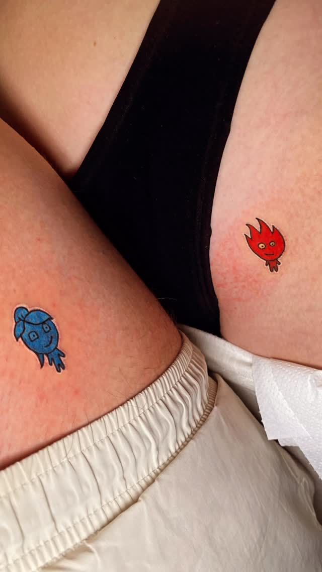 Dos pequeños tatuajes de pájaros de dibujos animados, azules y rojos, en los muslos adyacentes.