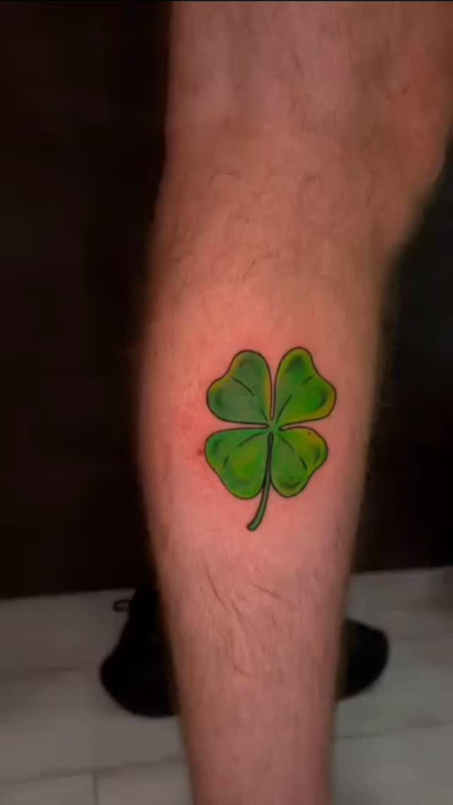 Tatuaje de trébol de cuatro hojas verde en la pantorrilla de una persona.