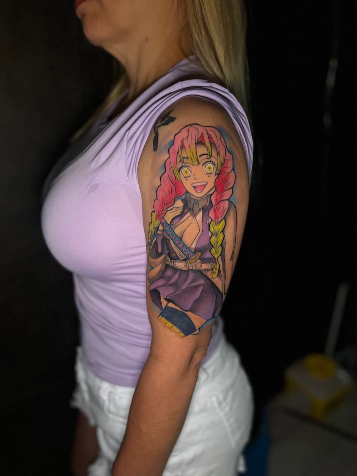 Mujer con un tatuaje del personaje de anime Mitsuri Kanroji en el brazo. Cabello rosa, traje morado y sonrisa.