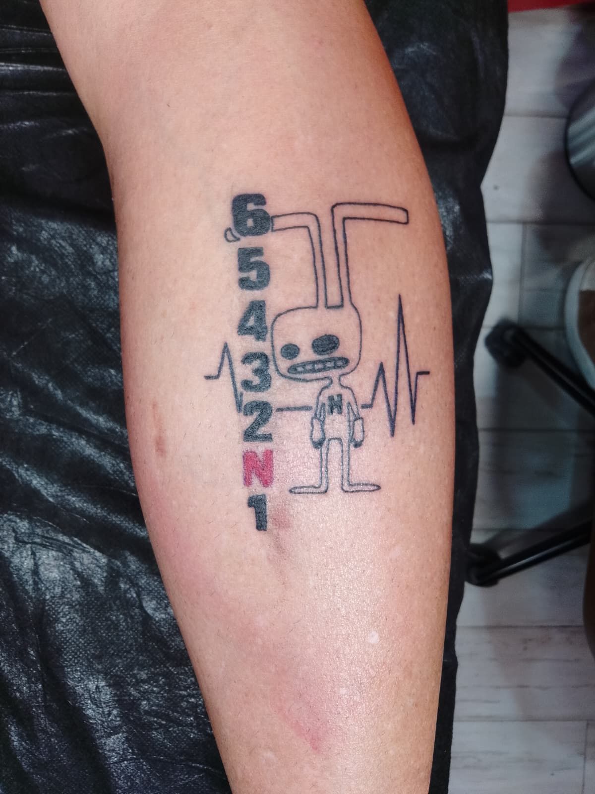 Tatuaje en el brazo: palanca de cambios, personaje de conejo con línea de latido del corazón.