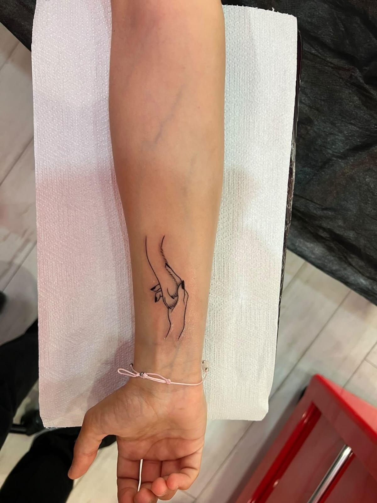 Tatuaje de dos manos, una sosteniendo a la otra en un antebrazo, tinta negra.