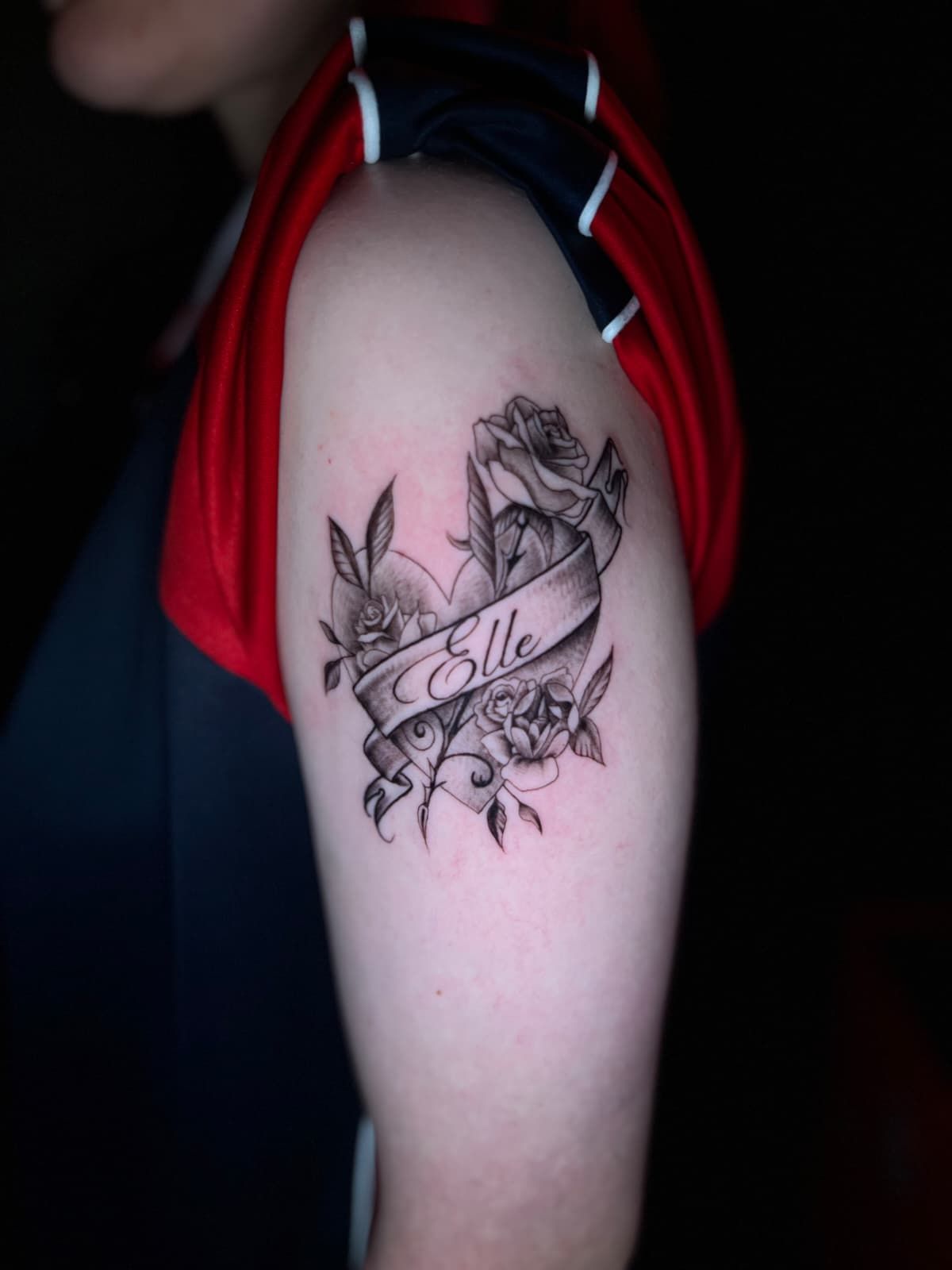 Tatuaje en la parte superior del brazo: una rosa, una pancarta con