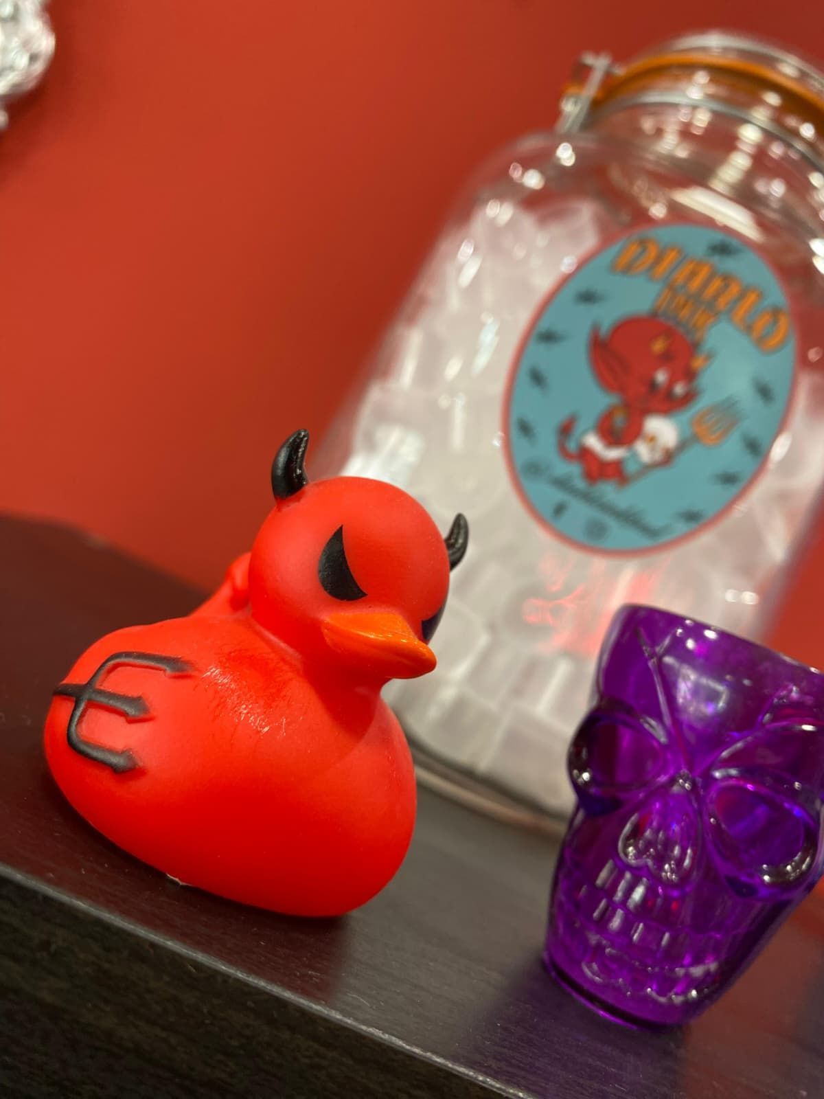 Pato diablo rojo, calavera morada, frasco de vidrio con etiqueta, sobre un fondo rojo.