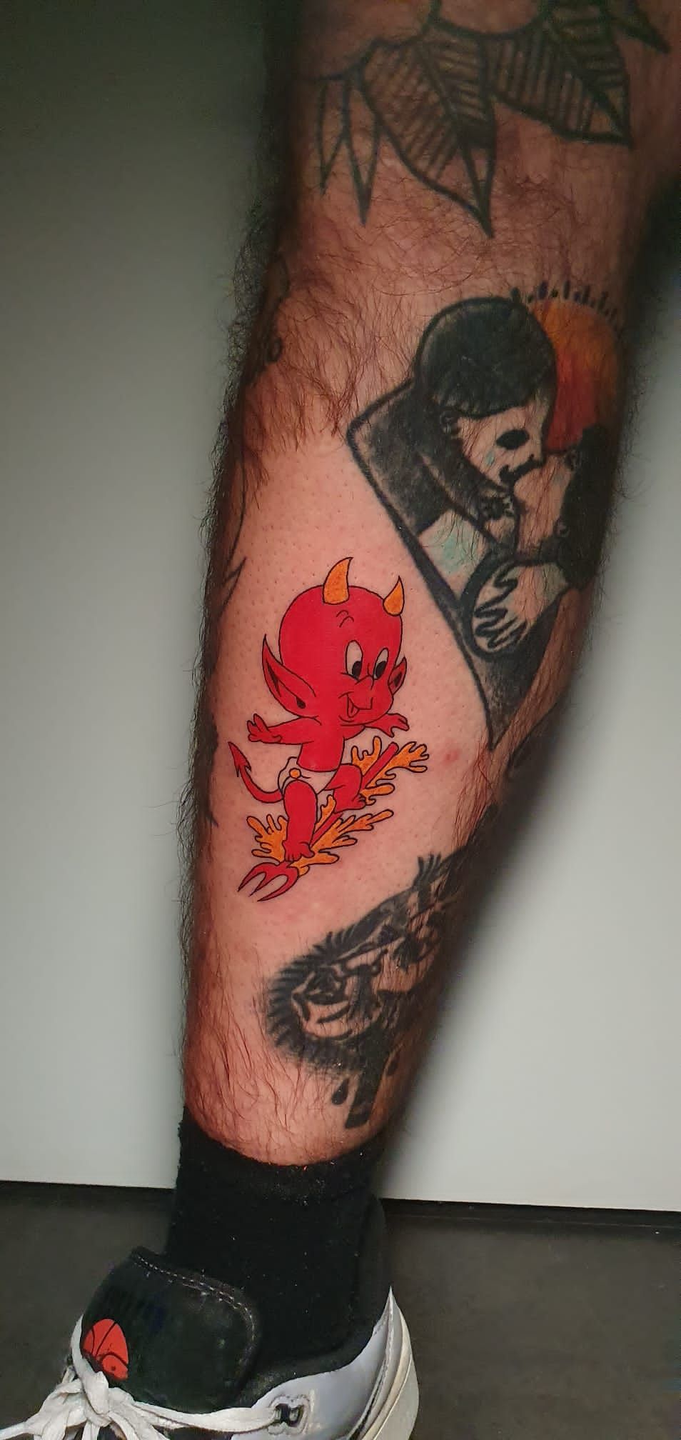 Pierna con múltiples tatuajes, incluido un diablo rojo, una persona con una capa y un lobo.