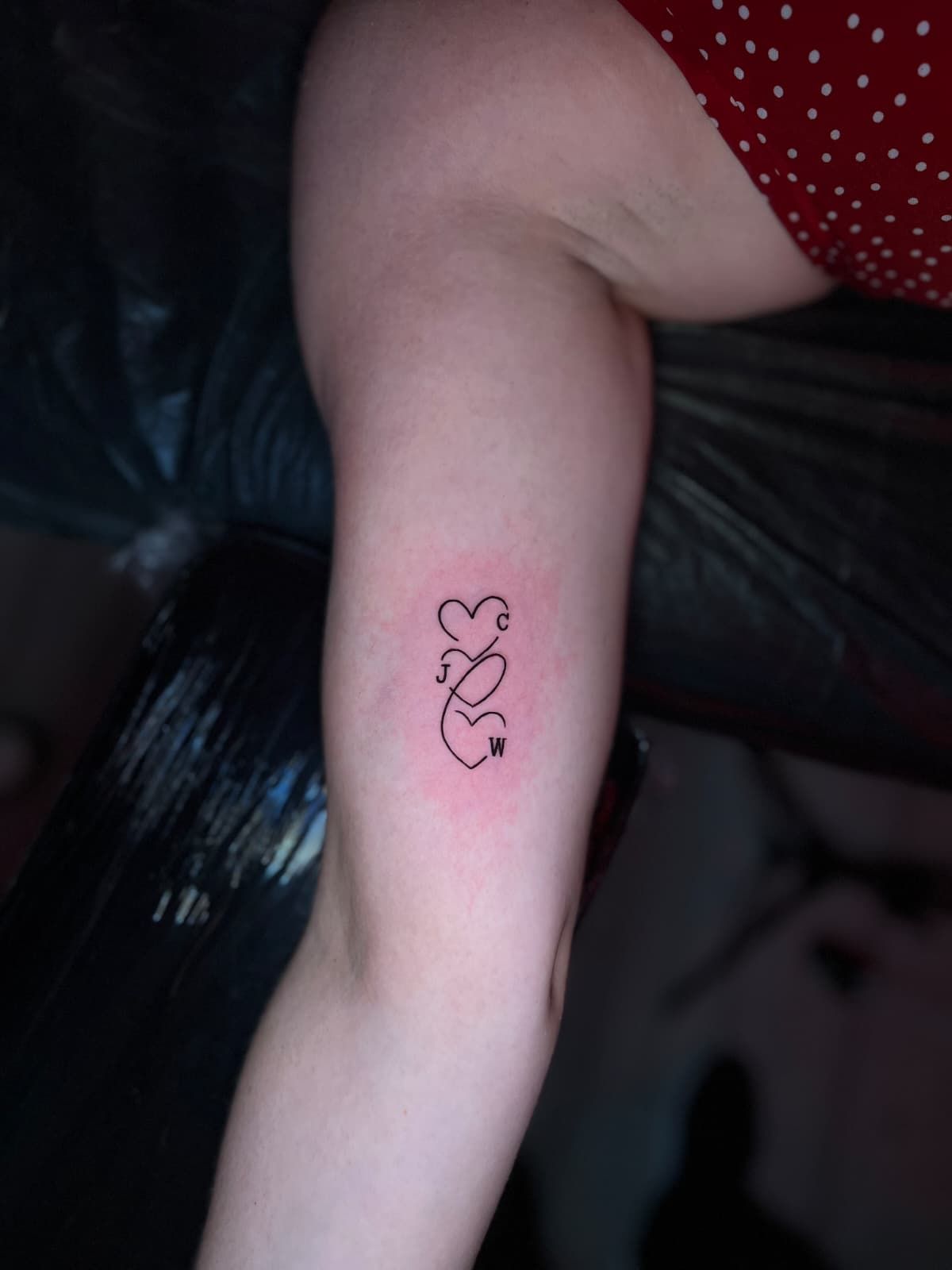 Brazo con un tatuaje minimalista de tres corazones conectados, posiblemente representando seres queridos, en tinta negra.
