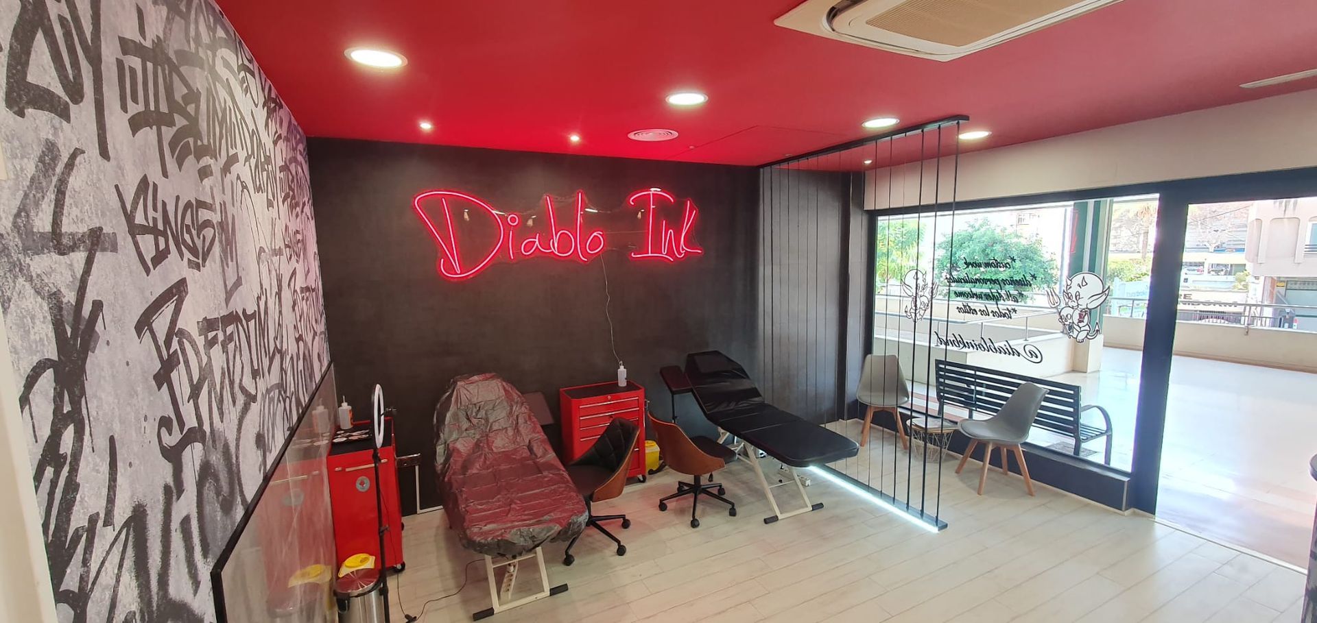 Interior de un salón de tatuajes, con decoración en rojo y negro, sillas de tatuaje y arte de graffiti.