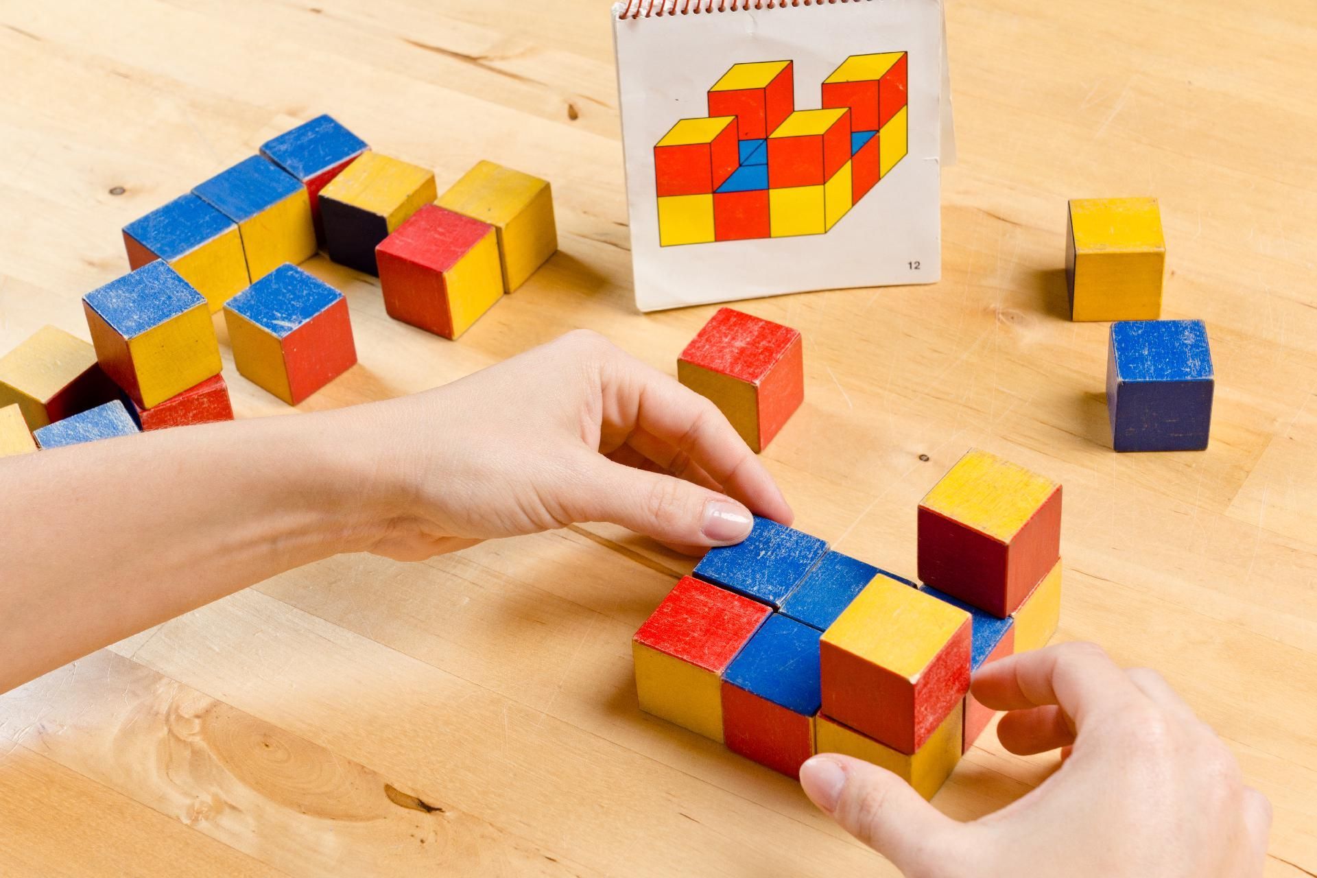 Eine Person mit einer weißen Handgelenkbandage übt die Hand-Augen-Koordination mit farbigen Stiften an zwei Stecktafeln.