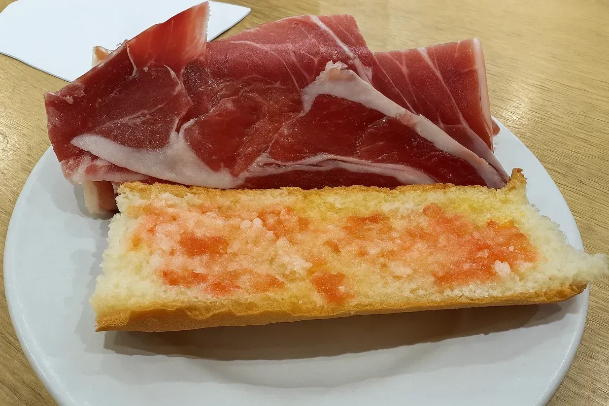 Plato de jamón lonchas y pan con cobertura de tomate.