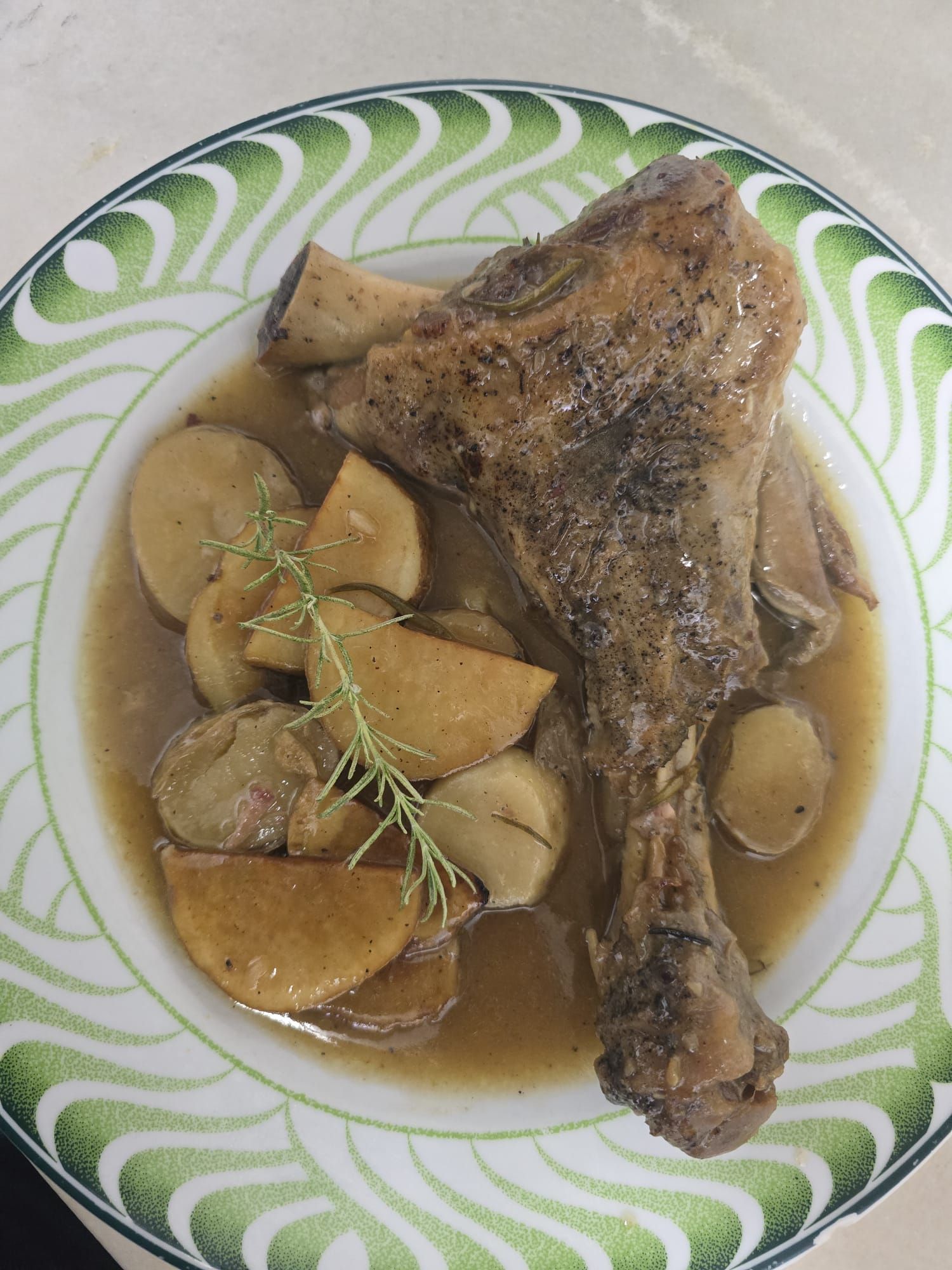 Pierna de cordero con patatas y romero en plato decorativo.