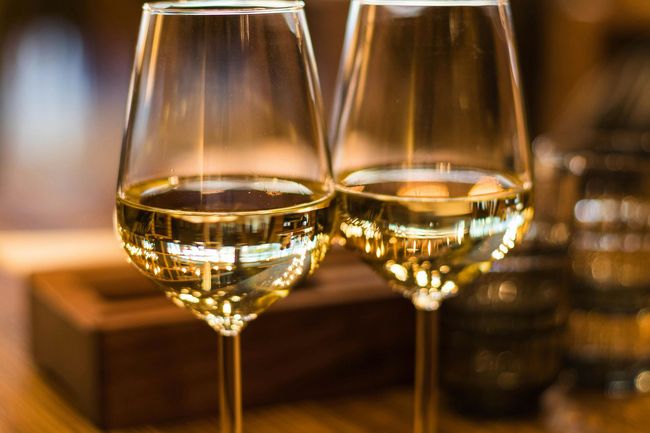 Dos copas de vino llenas de vino blanco sobre una mesa, reflejando el entorno.