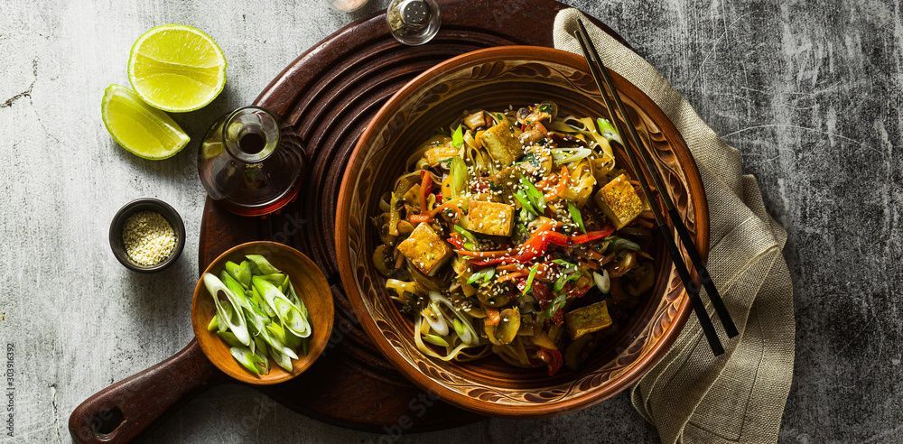 Schüssel mit gebratenem Tofu mit Limette, Sojasauce und Frühlingszwiebeln auf einem Holztablett.