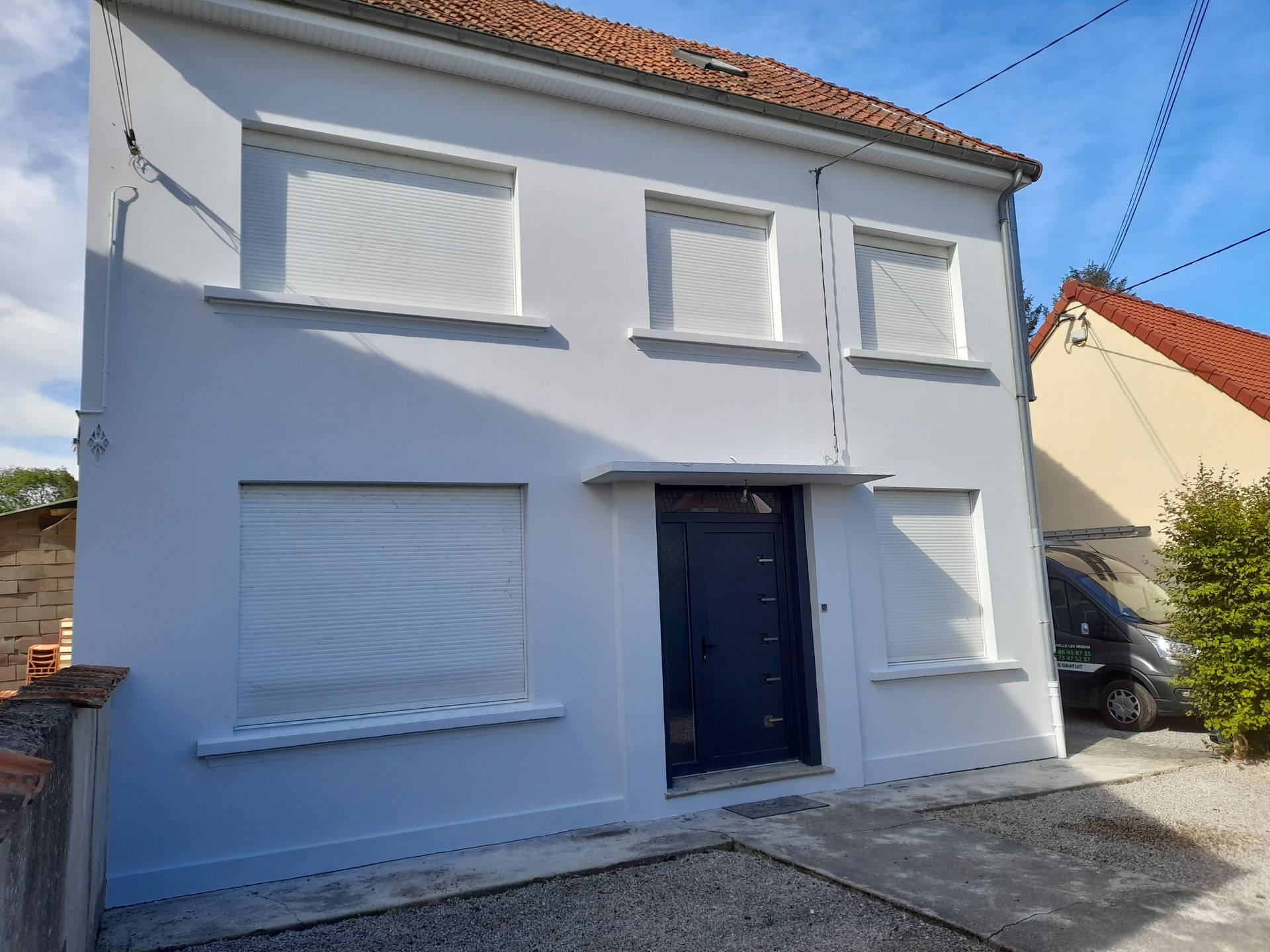 Façade avant d'une maison blanche avec volets roulants fermés