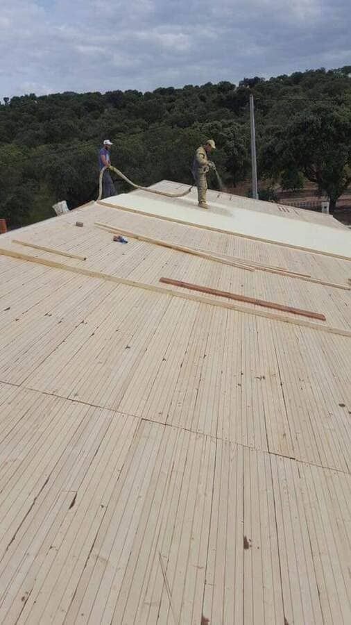 Dos hombres están trabajando en un techo de madera con árboles al fondo.