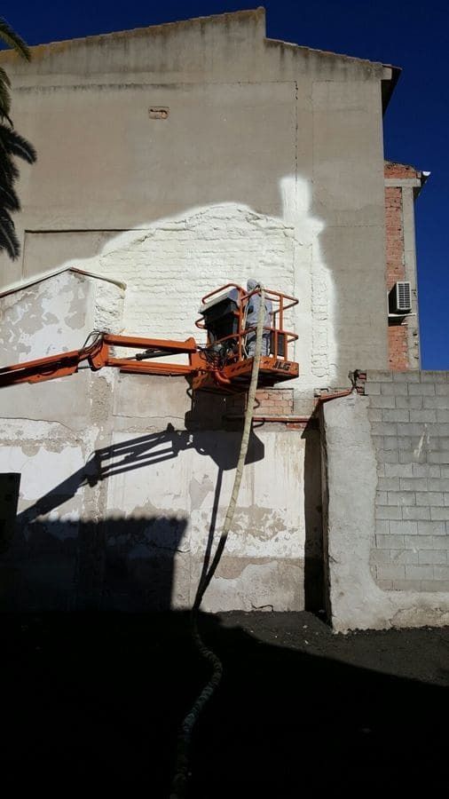 Un hombre está pintando el costado de un edificio con una grúa.