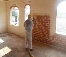Un hombre está rociando espuma sobre una pared de ladrillos en una habitación.
