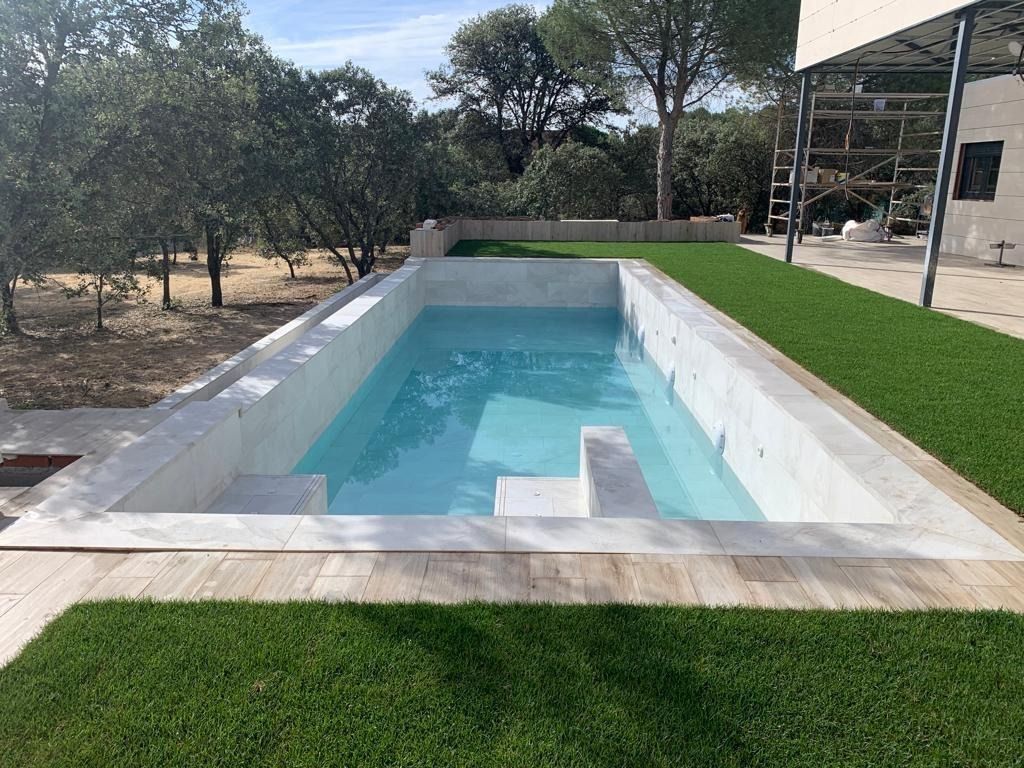 Una gran piscina rodeada de césped y árboles en un patio trasero.