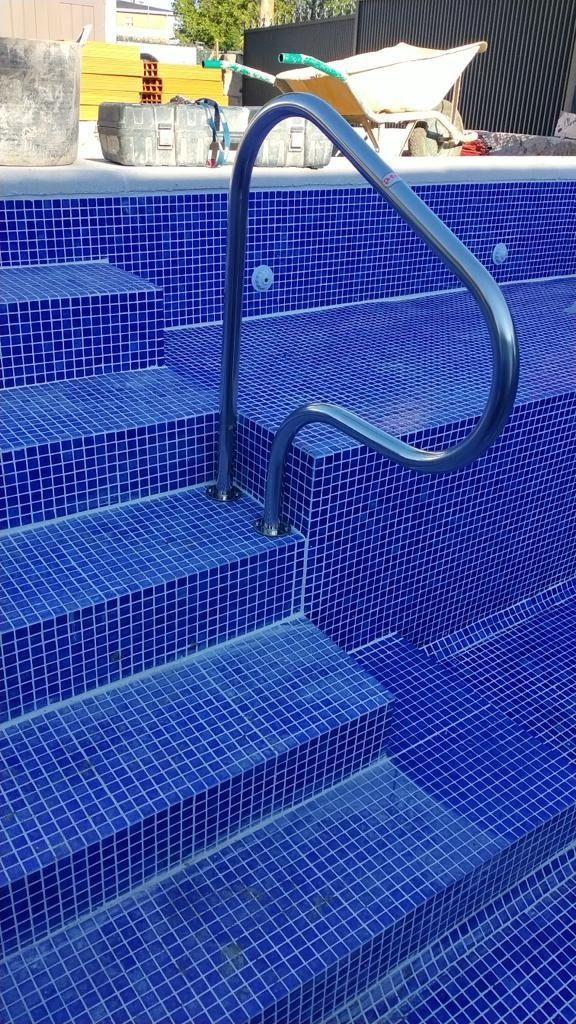 Una piscina con azulejos azules y barandilla metálica.
