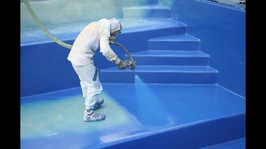 Un hombre está rociando pintura azul en una piscina.