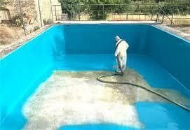 Un hombre está pintando una piscina con una manguera.