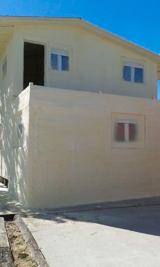 Una casa blanca con muchas ventanas y un cielo azul al fondo.