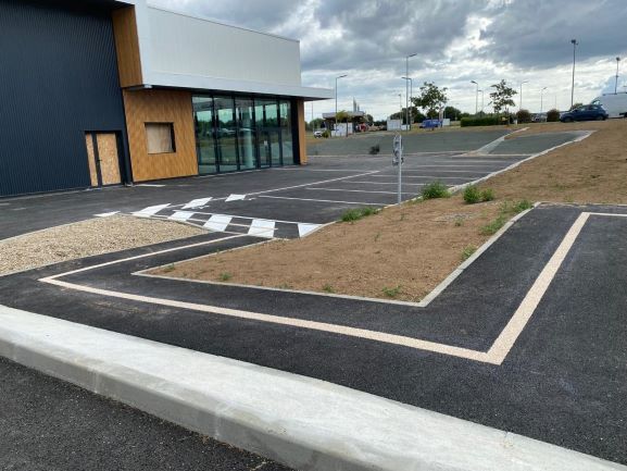 Marquage au sol en blanc pour des places de parking et la voie piétonne devant une structure professionnelle