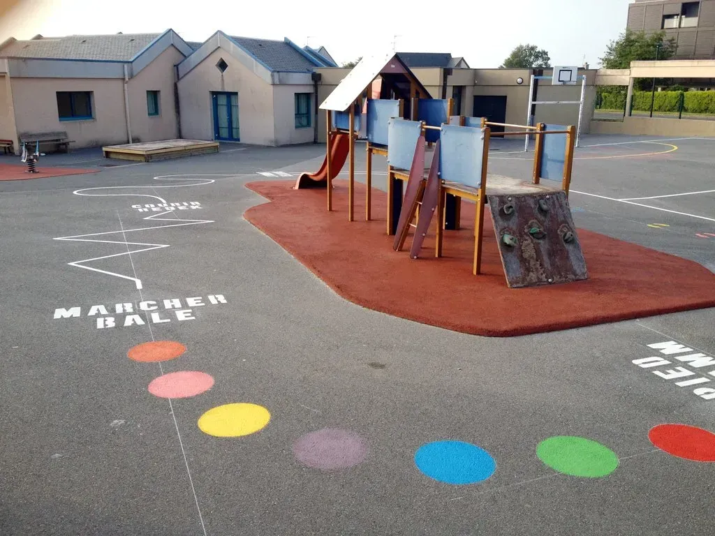 Marquage au sol de différentes couleurs autour d'un jeu pour enfant dans une cour d'école