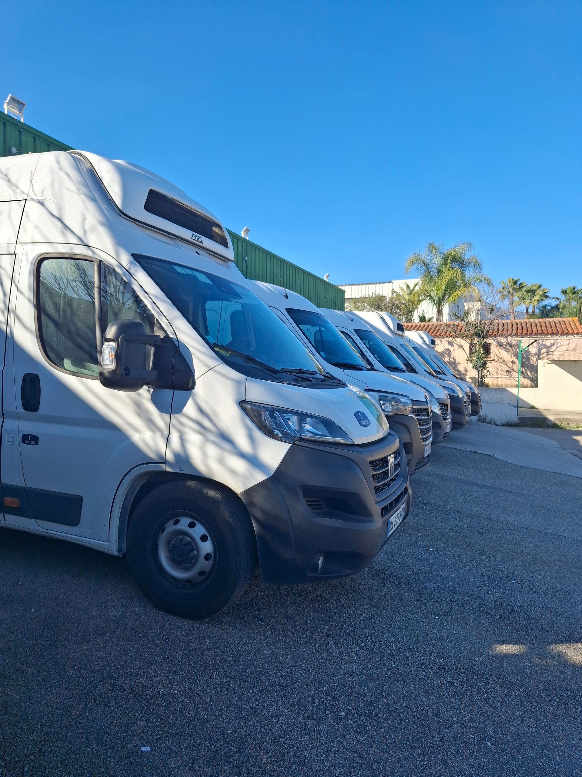 Présentoir de produits frais sur un marché : tomates, poivrons, aubergines et autres légumes. Caisses et paniers en bois.