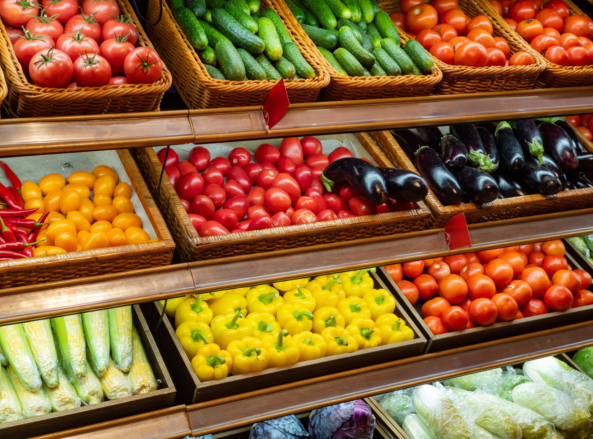 Présentoir de légumes dans un magasin, avec des tomates, des concombres, des aubergines et des poivrons dans des paniers.