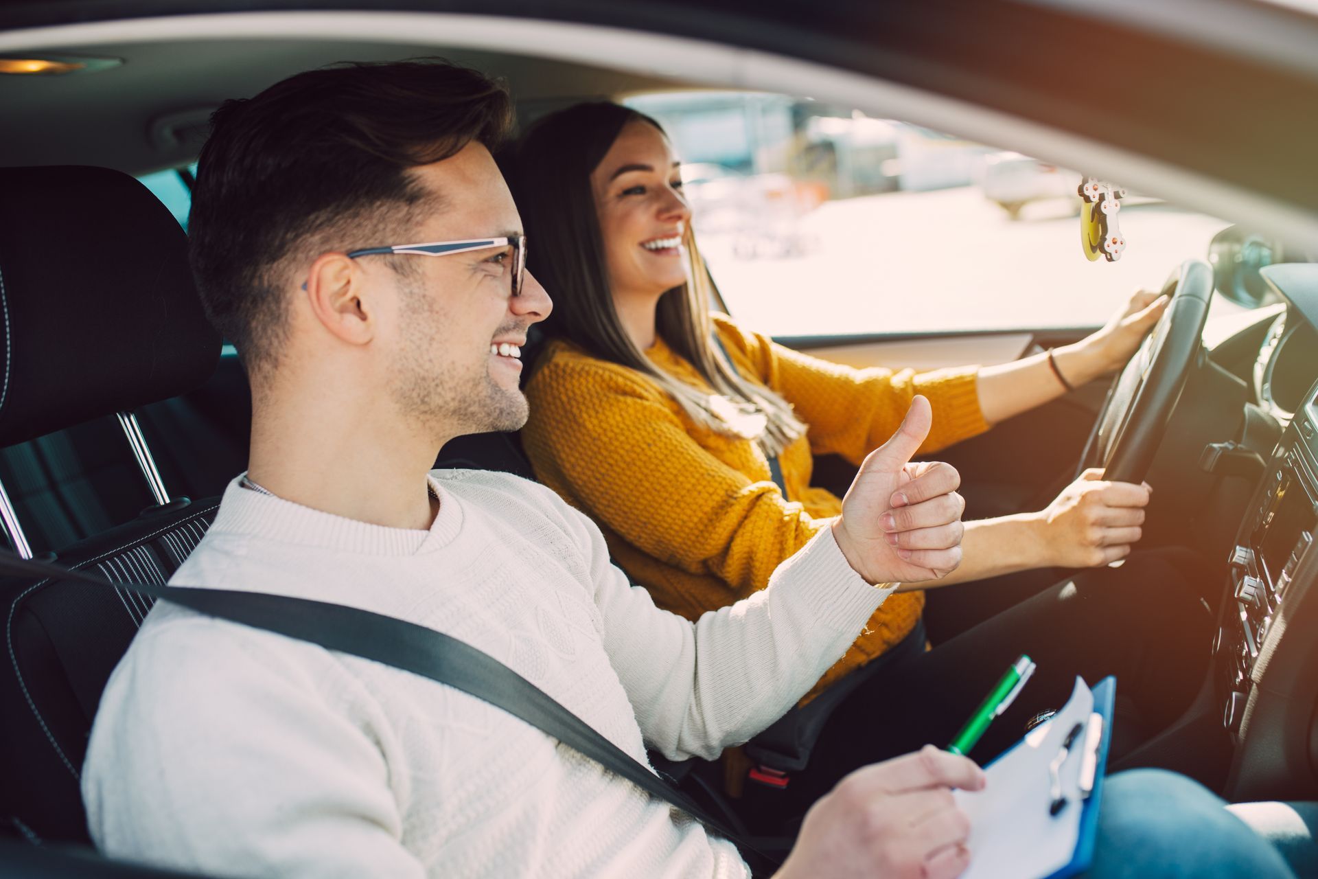 Une femme au volant, souriante, avec un instructeur levant le pouce ; à l'intérieur de la voiture.