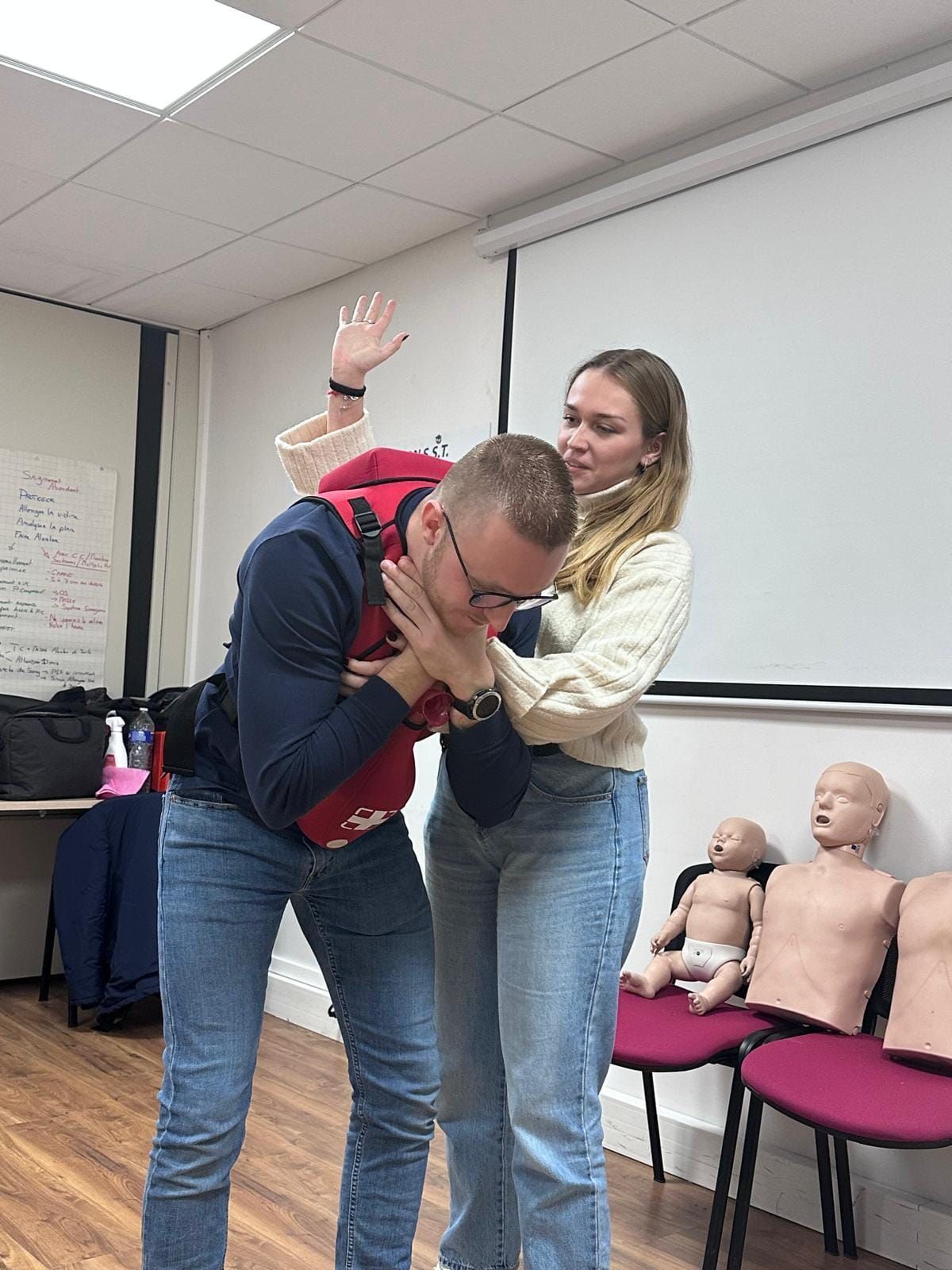 Une femme pratique la manœuvre de Heimlich sur un homme dans une salle de classe avec des mannequins.