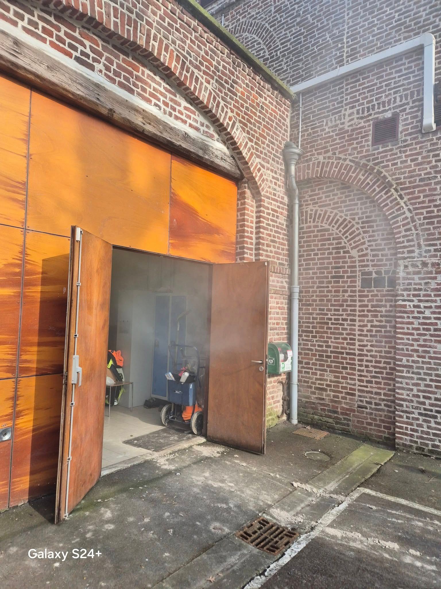 Des portes rouillées s'ouvrent, de la fumée et des pompiers se trouvent à l'intérieur d'un bâtiment en briques.