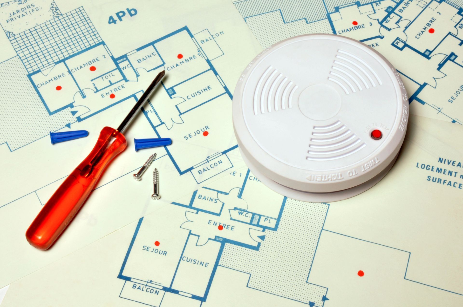 Détecteur de fumée, tournevis et vis sur des plans architecturaux.