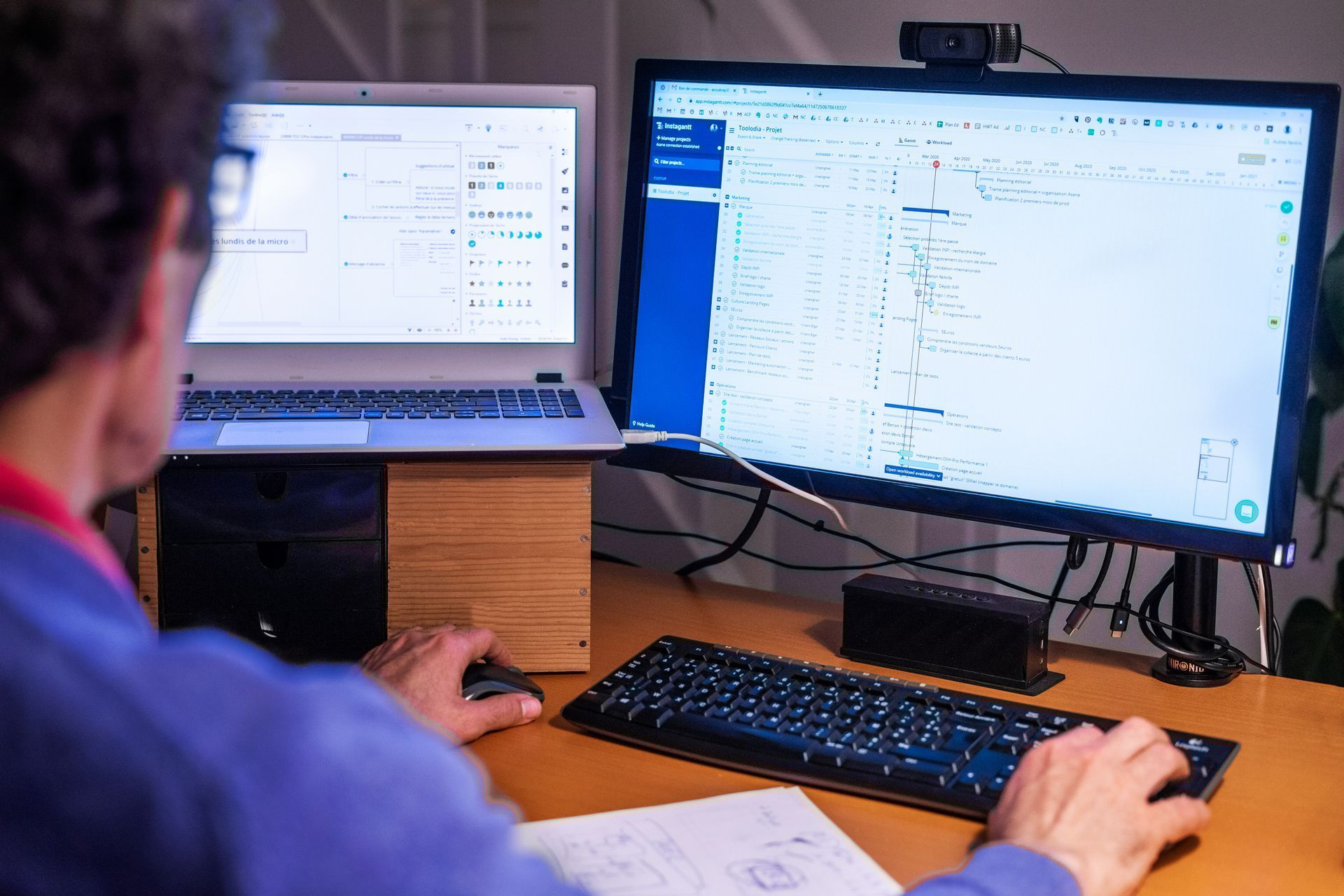 Une personne travaillant à un bureau équipé de deux écrans, d'un ordinateur portable et d'un clavier.