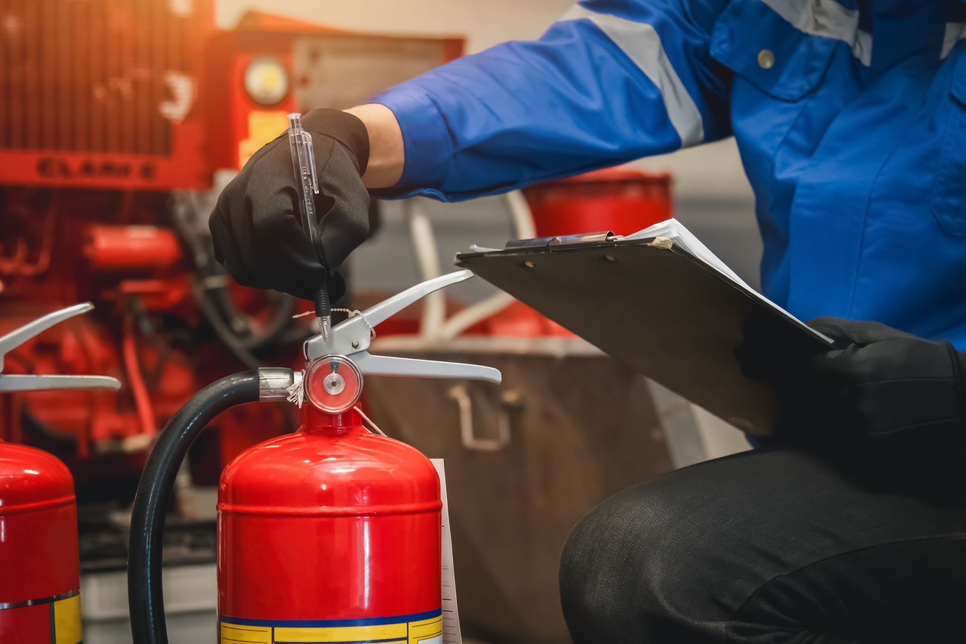 Une personne en uniforme bleu inspecte un extincteur rouge, tenant un bloc-notes.