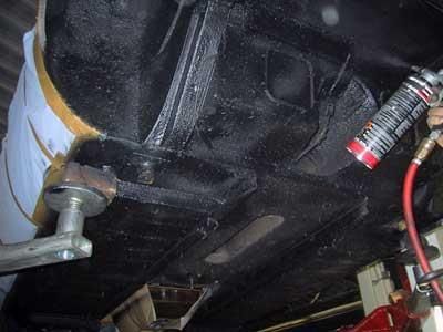 Eine Person sprüht aus einer Dose Farbe auf die Unterseite eines Autos.